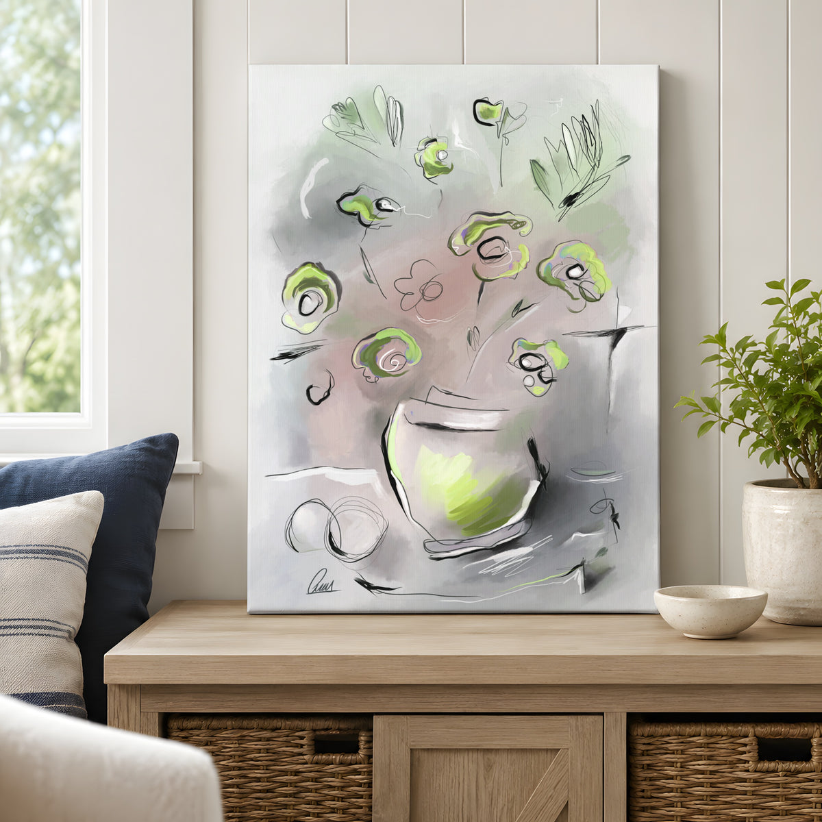 A vertical canvas art print featuring an abstract floral painting in shades of sage green, soft muted tones, and gray, styled on a light wood console table in a bright, modern living room setting.