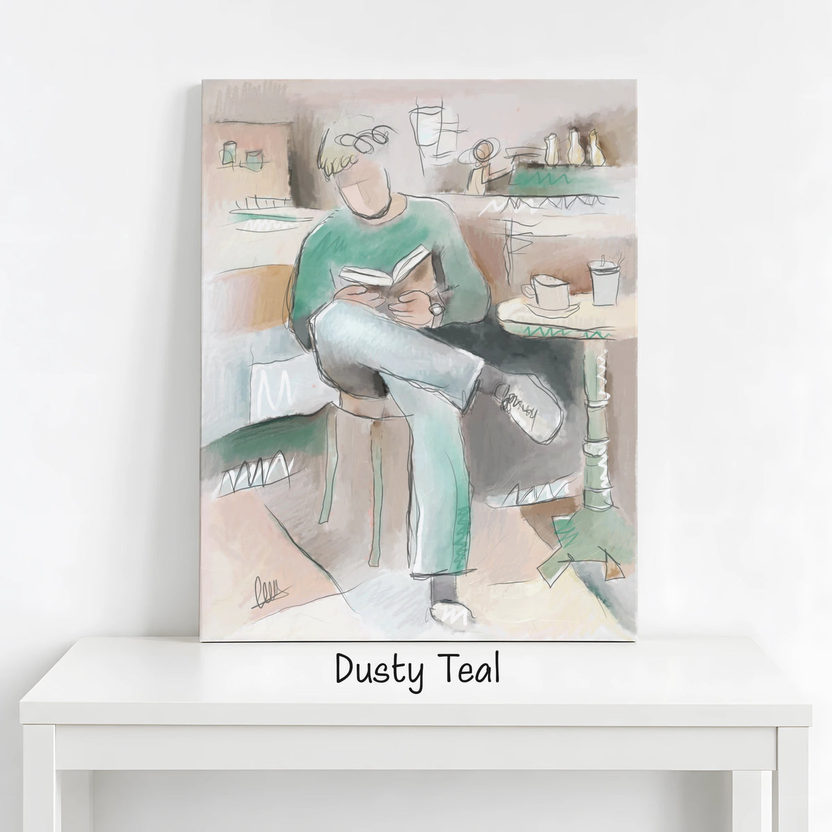 A vertical canvas art print depicting a person sitting and reading, styled in a cafe setting. The artwork is shown leaning against a white wall on a white table, with the text 'Dusty Teal' written below.